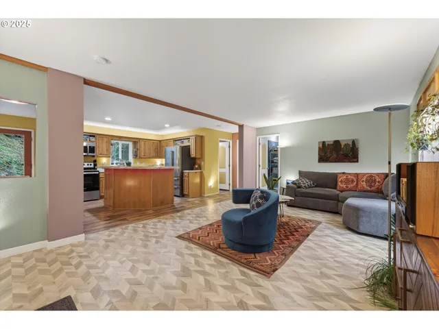 a living room with stainless steel appliances furniture wooden floor and a kitchen view
