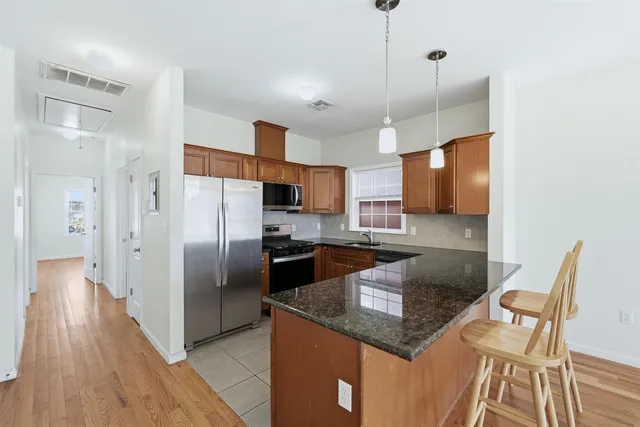 a kitchen with stainless steel appliances granite countertop a refrigerator a stove and a wooden floor