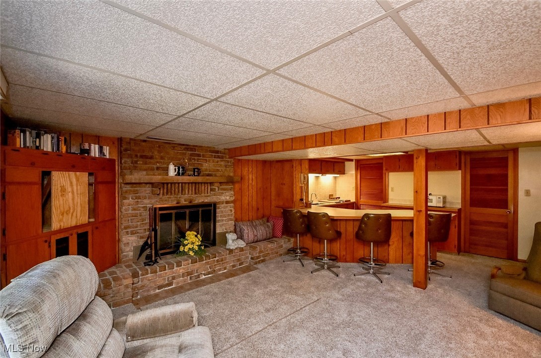 5653 Dailey Road New Franklin, OH 44319 - Photo 8 of 24 Carpeted living room featuring bar, a drop ceiling, wooden walls, and a fireplace