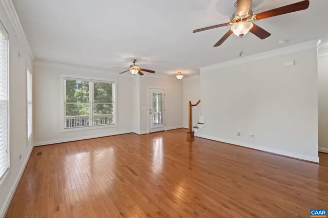 an empty room with wooden floor chandelier fan and windows