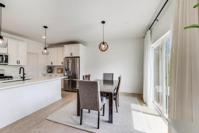 a kitchen with stainless steel appliances kitchen island granite countertop a dining table chairs and a refrigerator