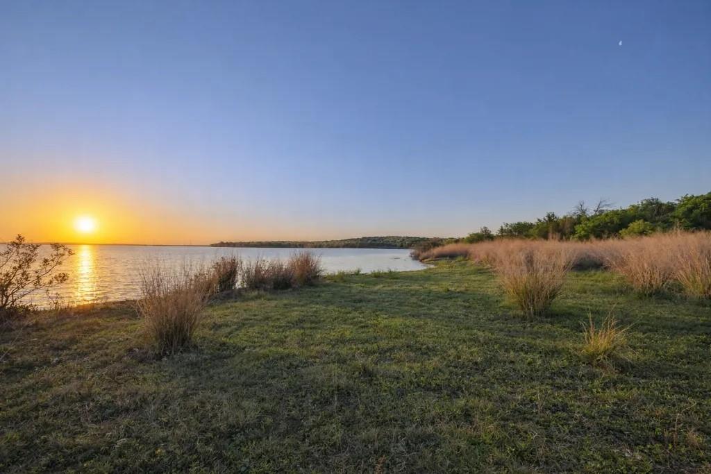 1180 McReynolds Road Sanger, TX 76266 - Photo 39 of 40 Expansive waterfront property featuring a calm body of water, a natural shoreline with green grass, and mature foliage bordering the horizon