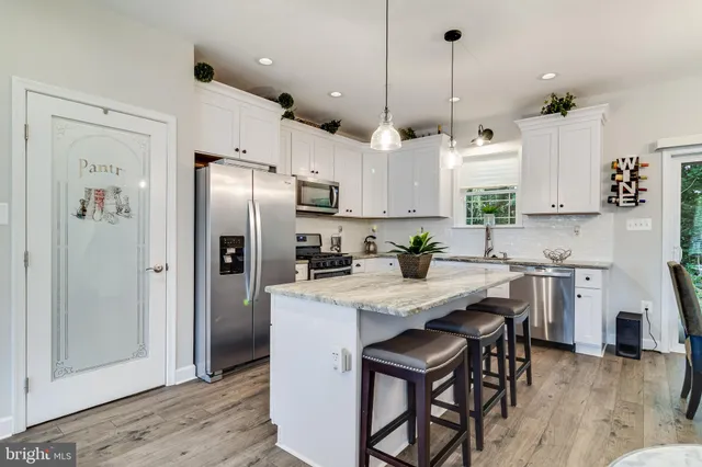 a kitchen with stainless steel appliances granite countertop a refrigerator a sink dishwasher a stove and white cabinets with wooden floor