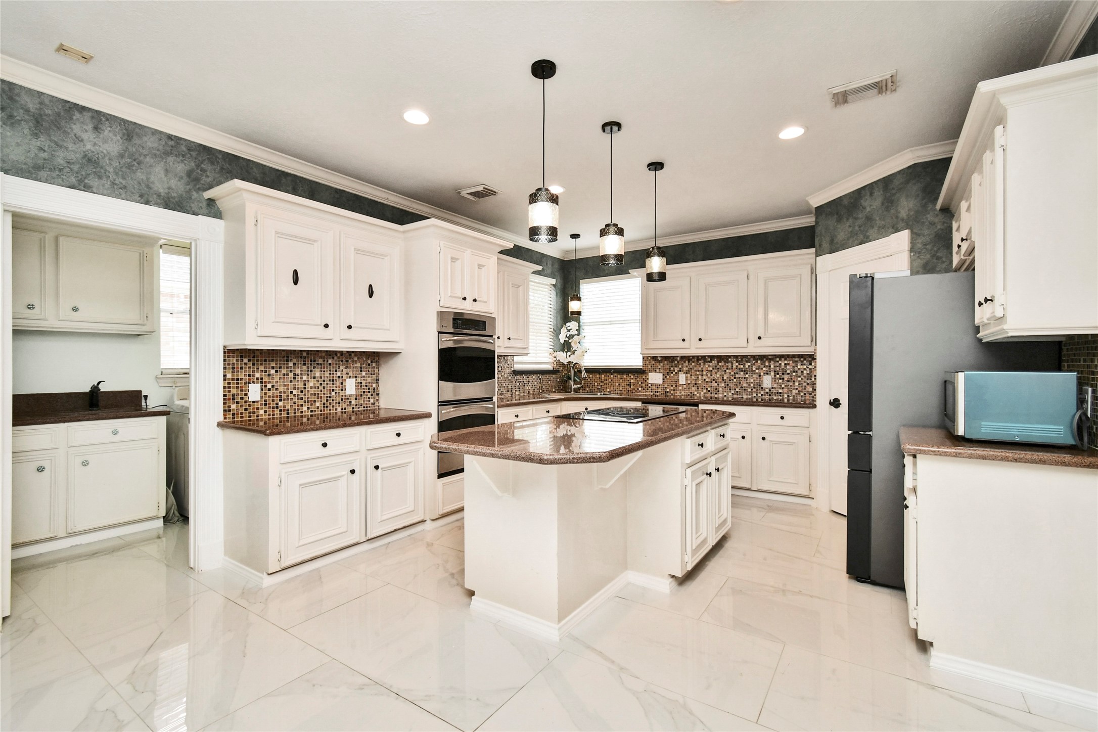 17311 Rothko Lane Spring, TX 77379 - Photo 13 of 37 Spacious kitchen with elegant white cabinetry, a large central island, and modern stainless steel appliances, accented by stylish pendant lighting and a mosaic tile backsplash.