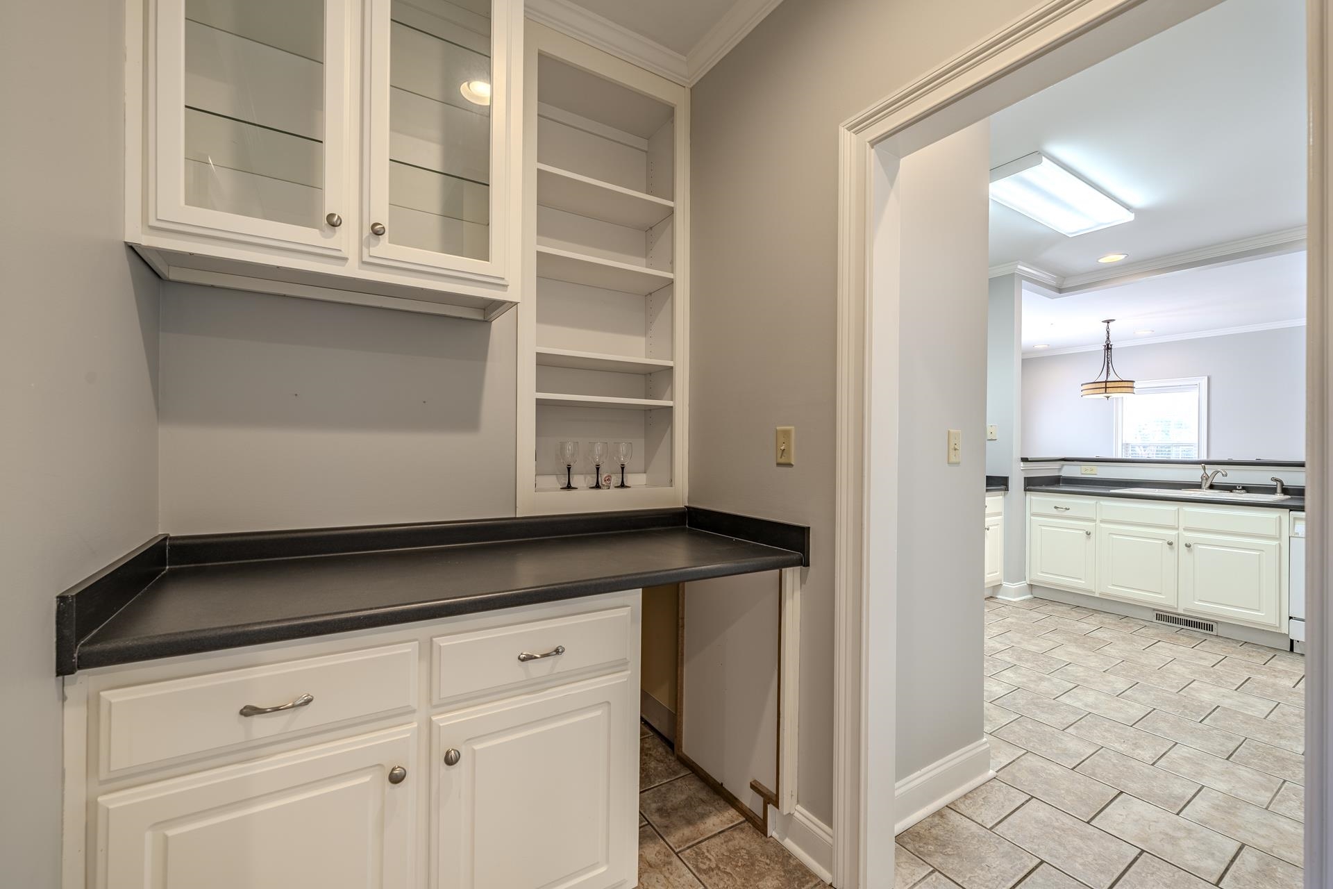 9 Mountain View Iuka, MS 38852 - Photo 10 of 32 Bar area with ornamental molding, white cabinets, dark countertops, glass insert cabinets, and light tile patterned floors