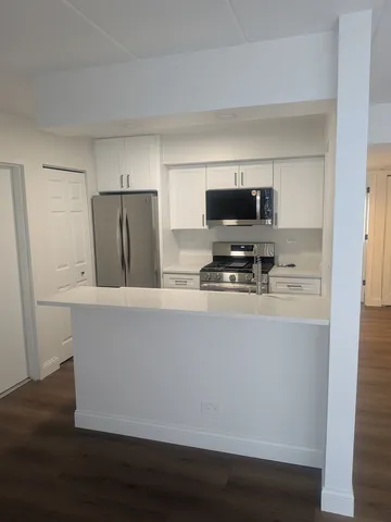 a living room with stainless steel appliances a refrigerator a stove a microwave and white cabinets