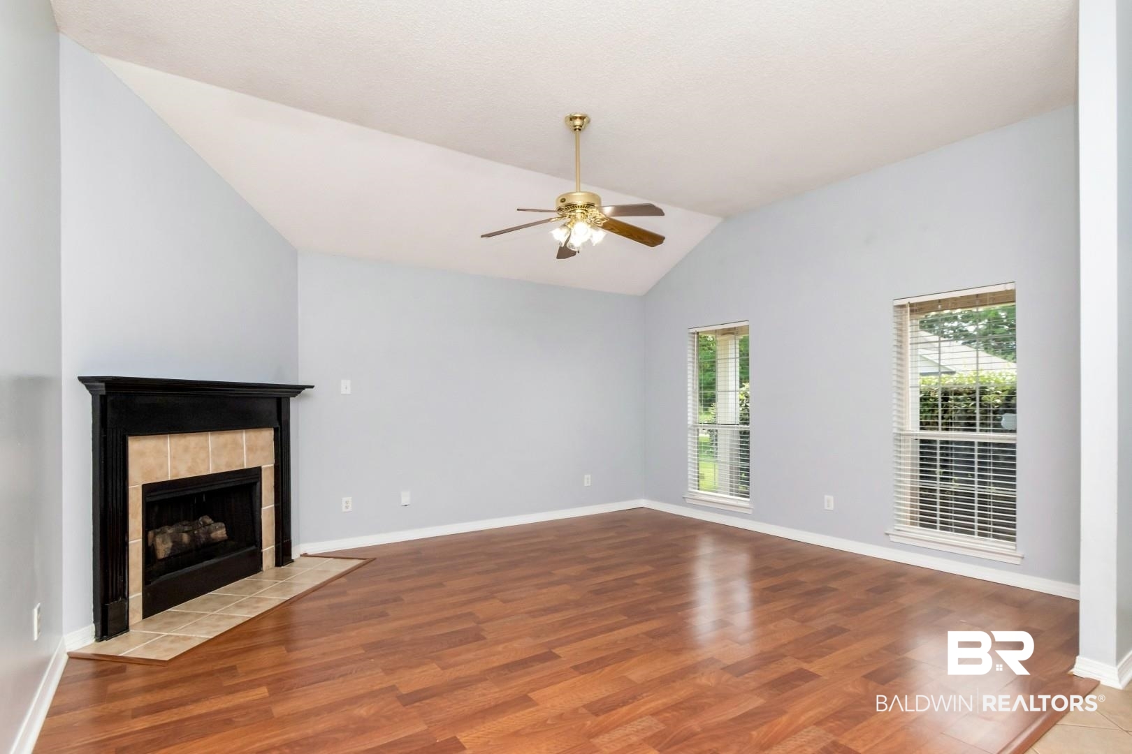 2136 Spring Grove Court Mobile, AL 36695 - Photo 6 of 38 Spacious room featuring wood-finish flooring, a vaulted ceiling, and a fireplace with a black wood mantel and tiled surround