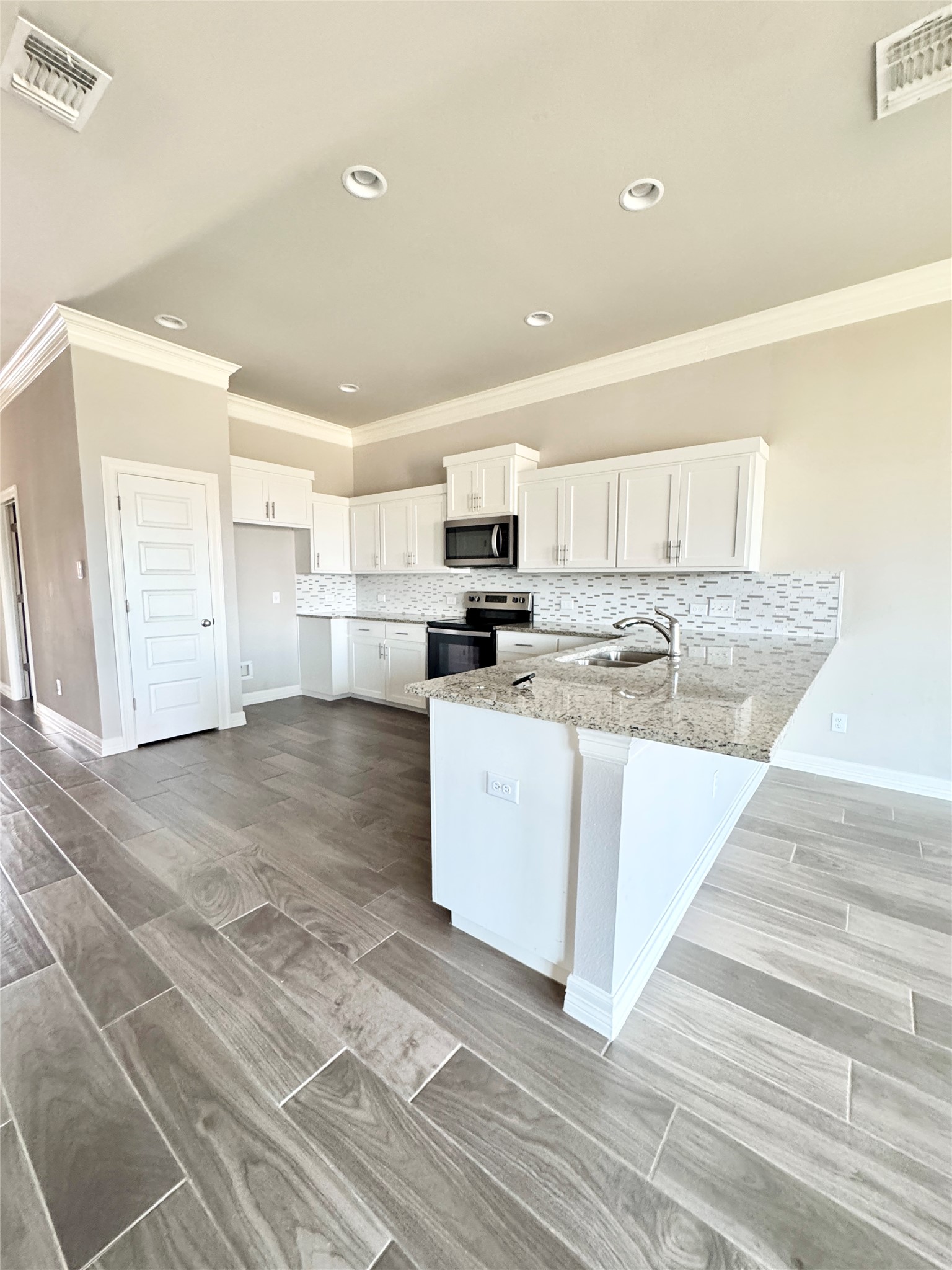 100 Bailey Kay Court, Unit B Jarrell, TX 76537 - Photo 12 of 14 Kitchen featuring a peninsula, light stone countertops, stainless steel appliances, white cabinets, and crown molding