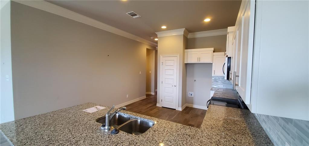 100 Bailey Kay Court, Unit B Jarrell, TX 76537 - Photo 4 of 14 Kitchen featuring white cabinets, light stone counters, a peninsula, dark wood finished floors, and stainless steel microwave