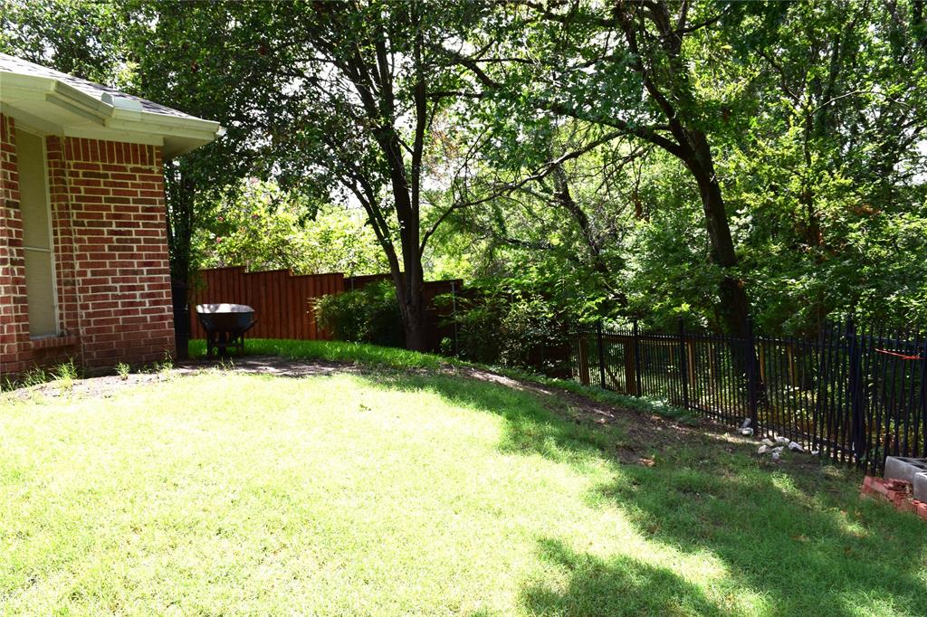 4201 Glistening Spring Rowlett, TX 75088 - Photo 32 of 33 Expansive backyard featuring a brick exterior, sloped lawn, a combination of wood and wrought iron fencing, and mature trees providing natural shading