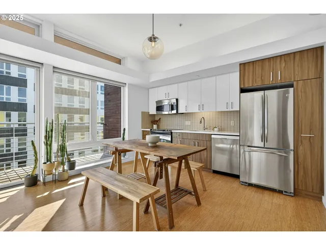 a kitchen with stainless steel appliances a stove a refrigerator a sink a stove and white cabinets with wooden floor