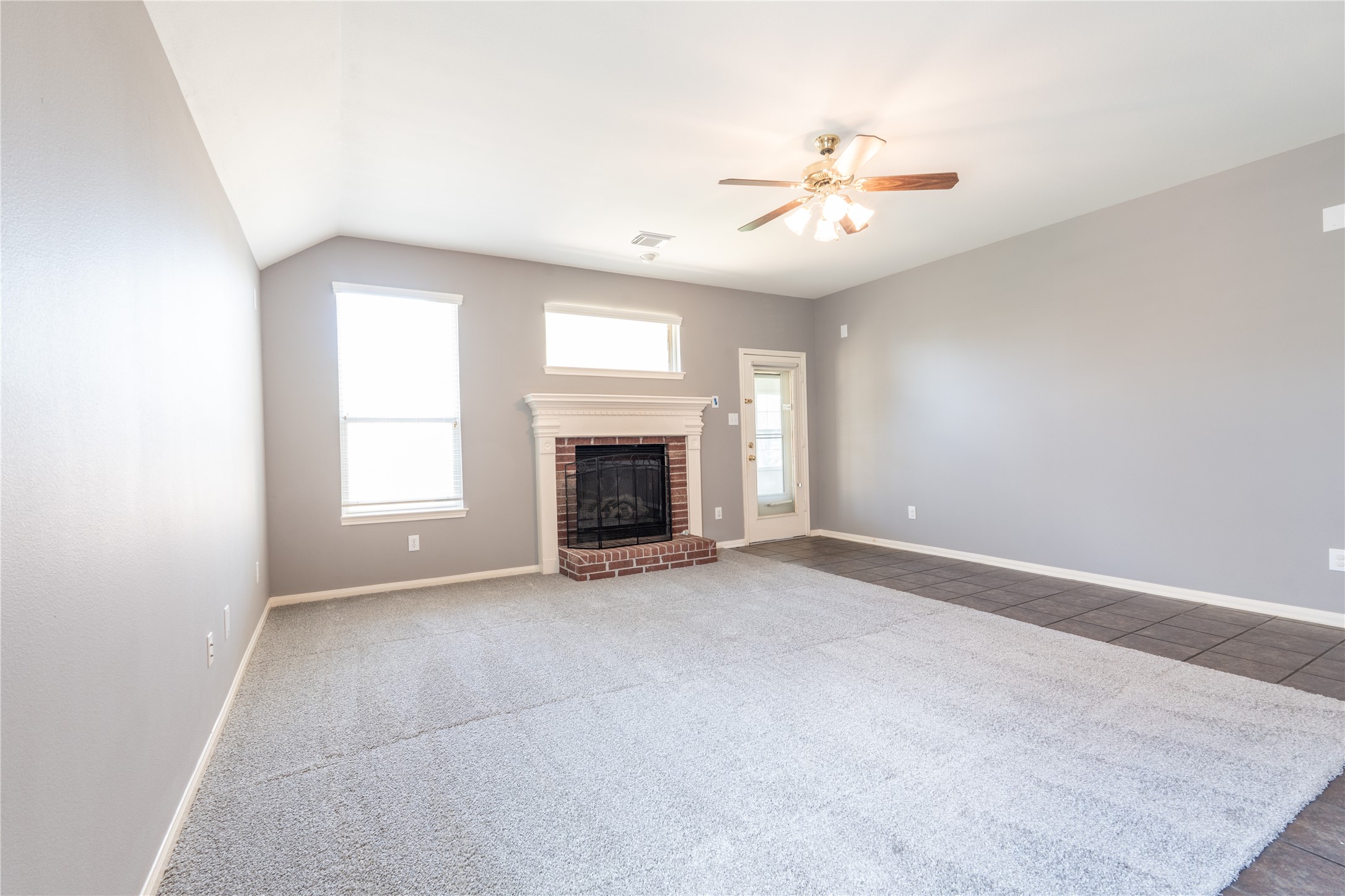 10619 Crownsedge Drive Spring, TX 77379 - Photo 9 of 38 This spacious living room features neutral gray walls, a cozy brick fireplace, and ample natural light from two windows. It has a ceiling fan and a combination of carpet and tile flooring, creating a warm and inviting atmosphere.