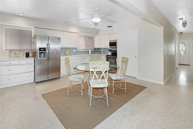 a dining area with stainless steel appliances kitchen island granite countertop a dining table chairs and a refrigerator