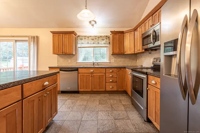 a kitchen with stainless steel appliances granite countertop a sink a stove top oven a refrigerator cabinets and a window