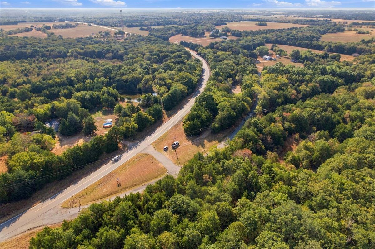 Bloomfield Road Colbert, OK 74733 - Photo 16 of 25 Expansive rural landscape featuring a paved road, abundant mature trees, and a distant water tower