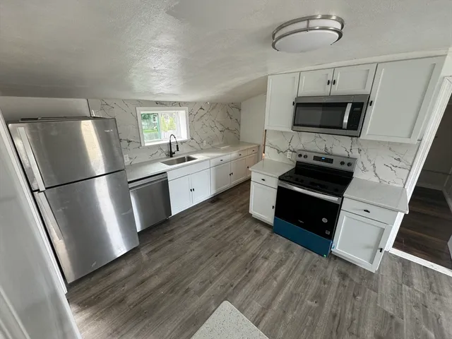 a kitchen with stainless steel appliances a refrigerator a stove a sink and white cabinets