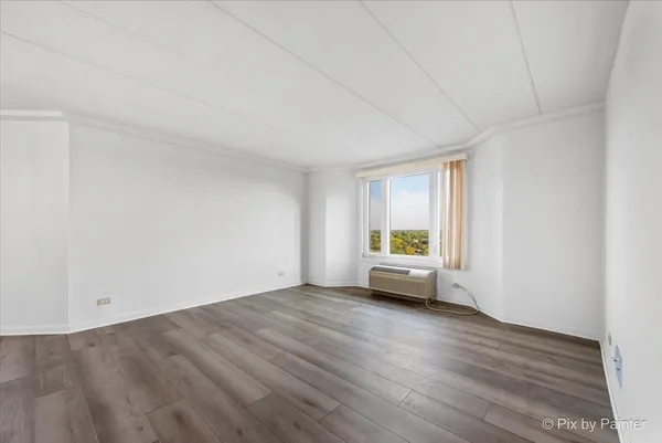 a view of an empty room with wooden floor and a window