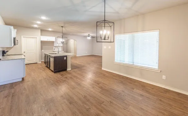 a view of empty room with wooden floor and kitchen view