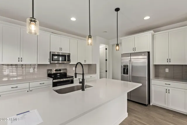 a kitchen with stainless steel appliances kitchen island granite countertop a refrigerator a stove a sink and white cabinets with wooden floor