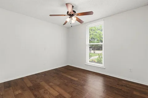 an empty room with wooden floor chandelier fan and windows