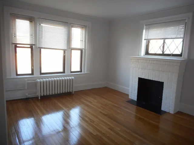 an empty room with wooden floor fireplace and windows