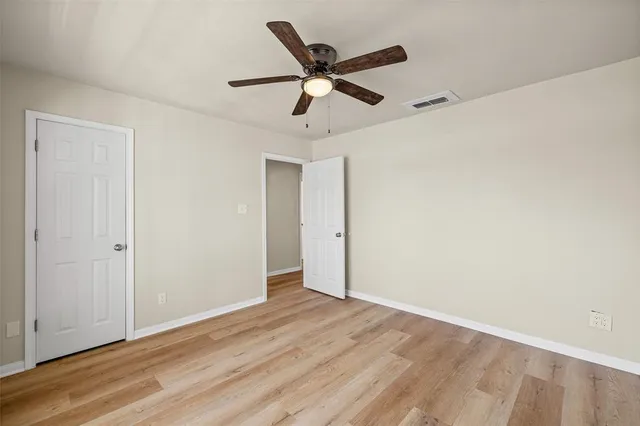 an empty room with wooden floor ceiling fan and windows