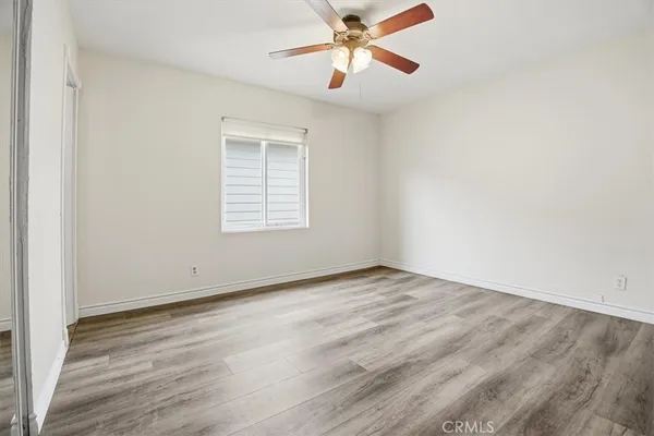 a view of an empty room with wooden floor and a ceiling fan