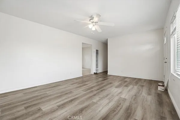 an empty room with wooden floor chandelier fan and windows