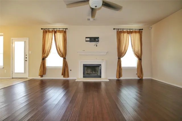 a view of an empty room with wooden floor fireplace and a window