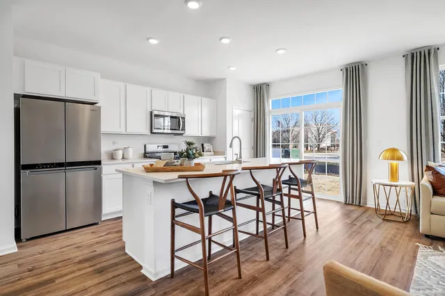 a kitchen with stainless steel appliances granite countertop a dining table chairs refrigerator and sink