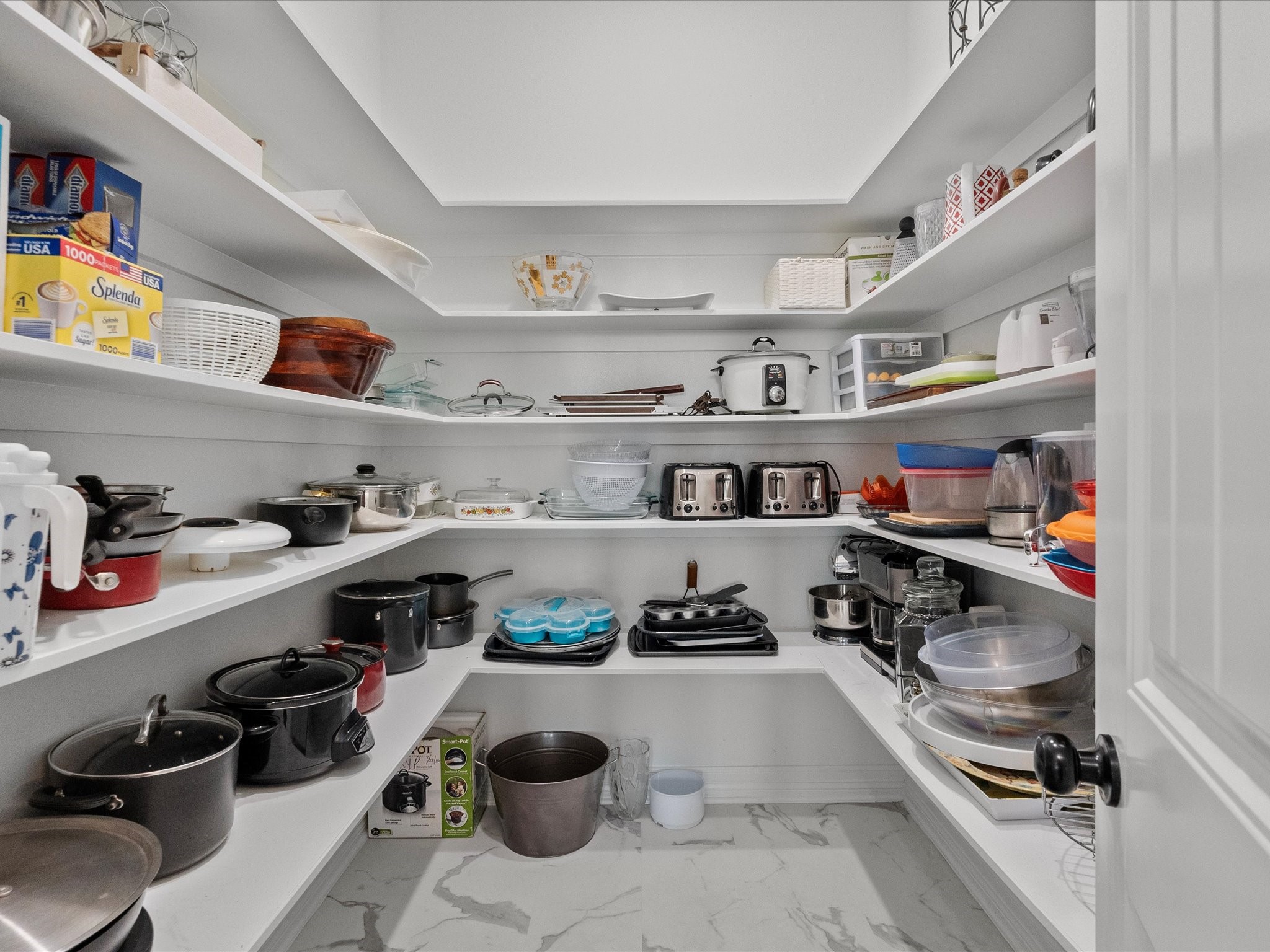 1018 Seashell Drive Surfside Beach, TX 77541 - Photo 23 of 49 This photo showcases a spacious, well-organized pantry with wrap-around white shelving, ample storage for kitchen appliances, cookware, and pantry items, and a clean, bright aesthetic.