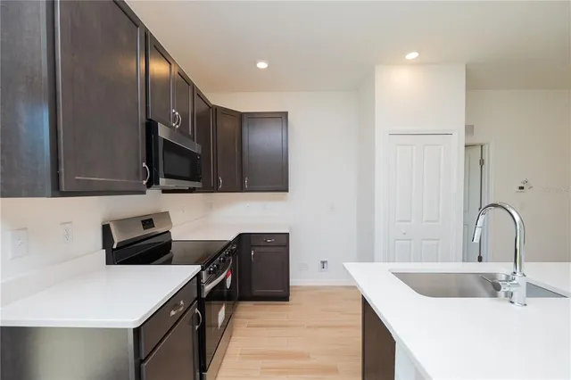 a kitchen with stainless steel appliances a sink dishwasher stove and microwave with wooden floor