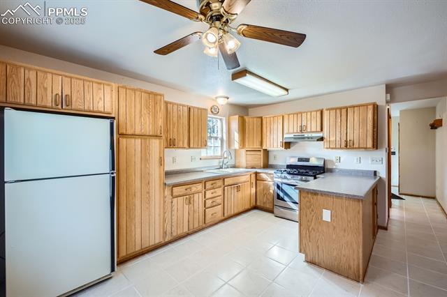 Kitchen featuring refrigerator, sink, ceiling fan, gas stove, and light brown cabinets