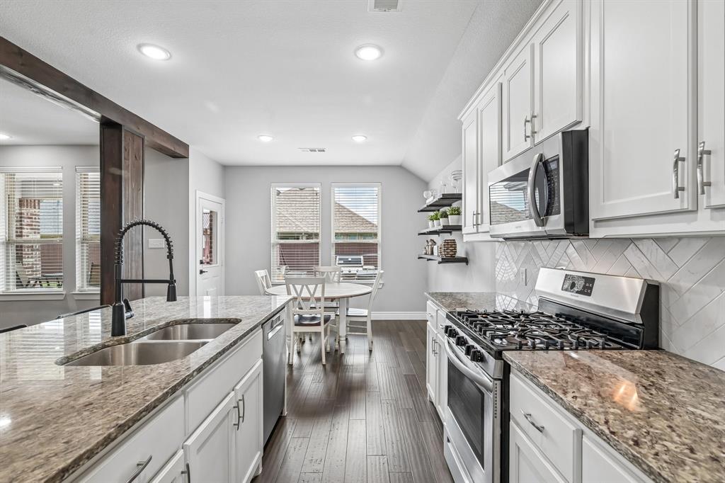 1805 Huntsman Way Forney, TX 75126 - Photo 11 of 34 Contemporary kitchen featuring white cabinetry, stone countertops, stainless steel appliances, a herringbone tile backsplash, and dark wood-finish flooring