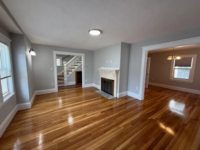 a view of an empty room with wooden floor fireplace and a window