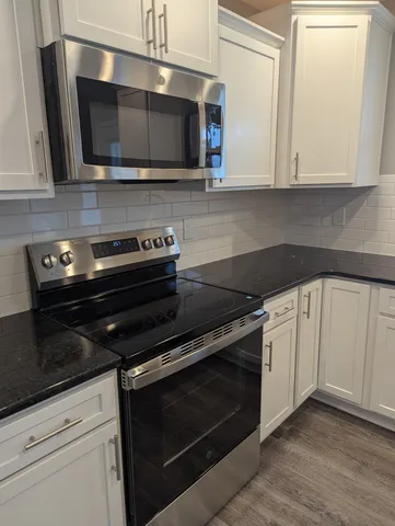 a kitchen with granite countertop white cabinets stainless steel appliances and wooden floor
