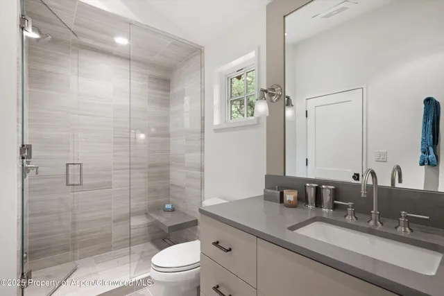 a bathroom with a granite countertop sink a toilet a large mirror and shower