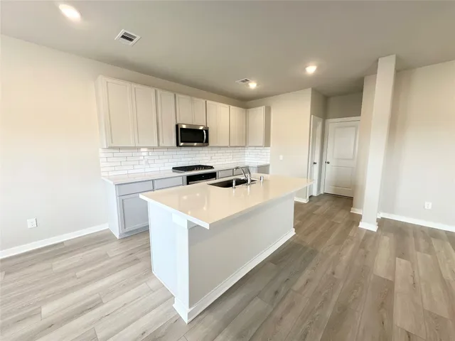 a view of an empty room with wooden floor and a kitchen