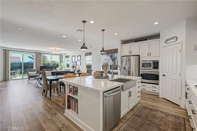 a open kitchen with stainless steel appliances granite countertop a stove a sink a dining table chairs and couches with wooden floor