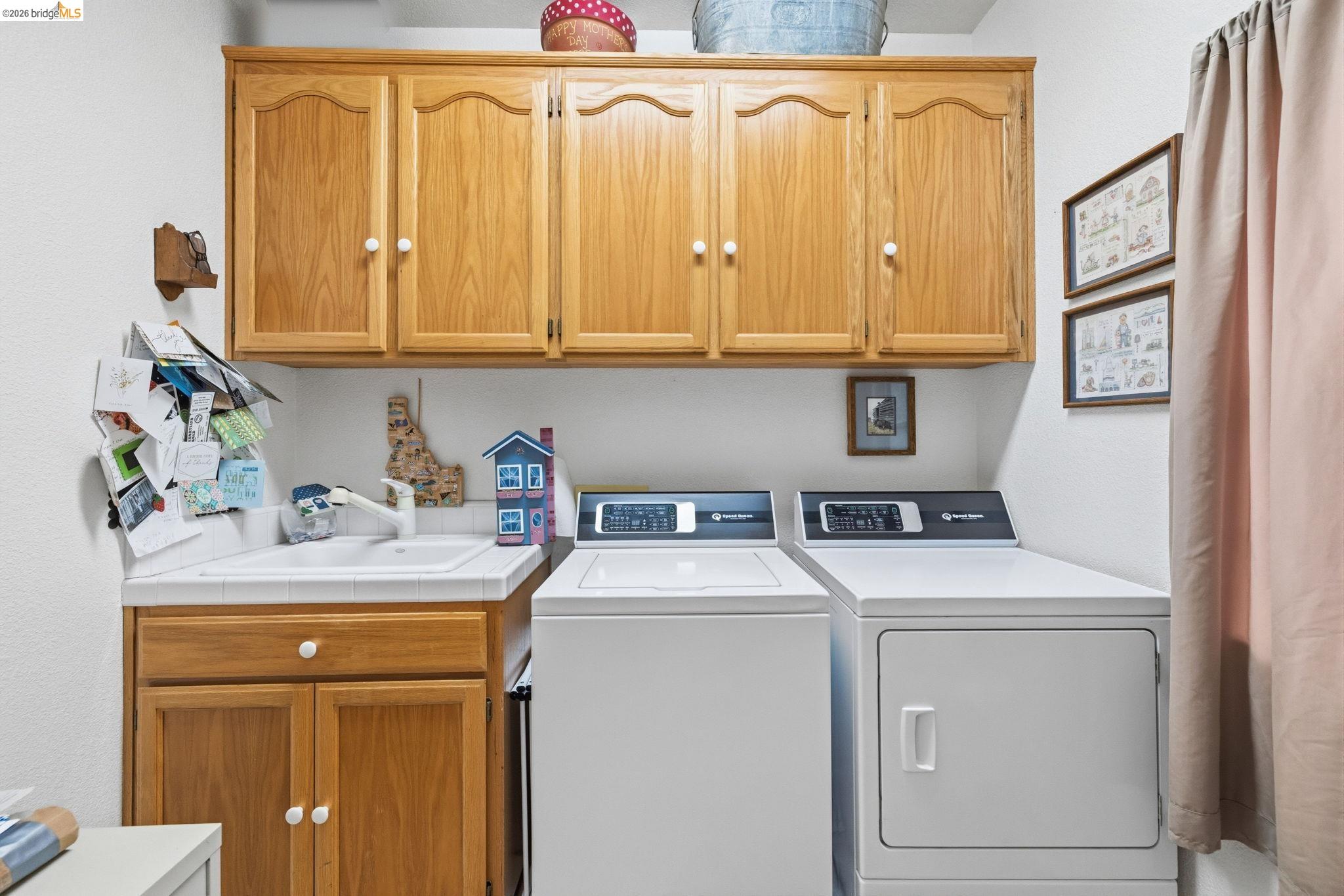 18450 Lambert Lake Road Sonora, CA 95370 - Photo 43 of 87 Laundry area featuring wood cabinetry, a utility sink with a white tiled countertop, and ample overhead storage