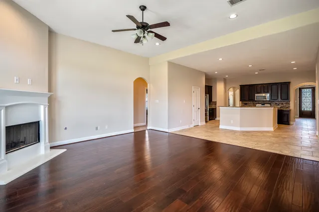 a view of an empty room with wooden floor and a kitchen