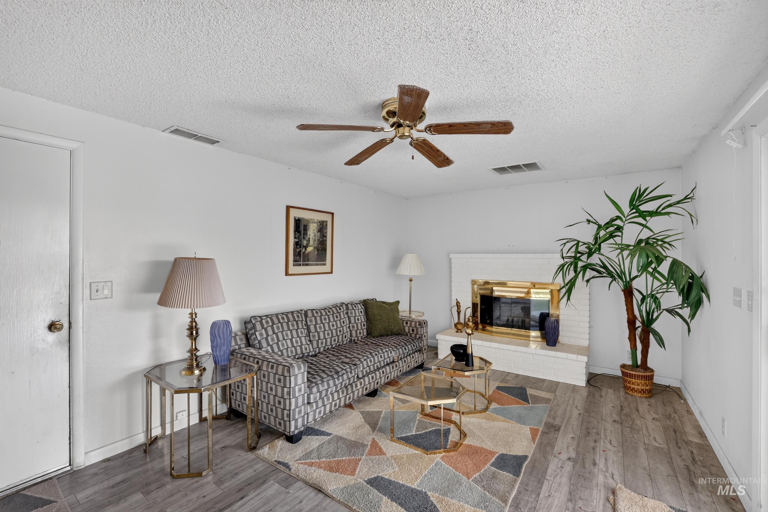 9055 West Highlander Road Boise, ID 83709 - Photo 16 of 39 Wood-finish flooring, white painted walls, and a white brick fireplace with a golden firebox