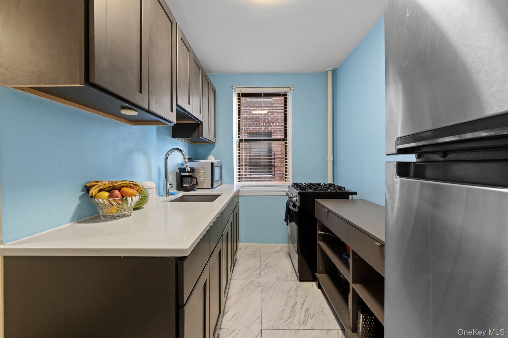 2830 Briggs Avenue, Unit 4F Bronx, NY 10458 - Photo 7 of 16 Kitchen featuring freestanding refrigerator, black gas stove, light marble finish flooring, light stone countertops, and dark brown cabinetry