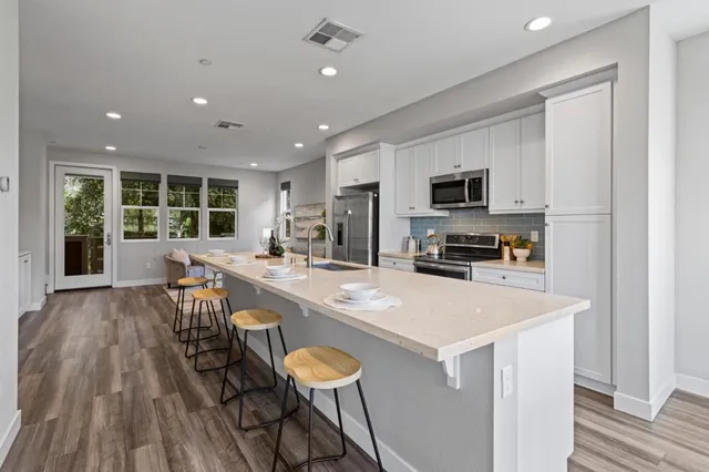 a kitchen with stainless steel appliances granite countertop a stove top oven a refrigerator a sink and a dining table with wooden floor