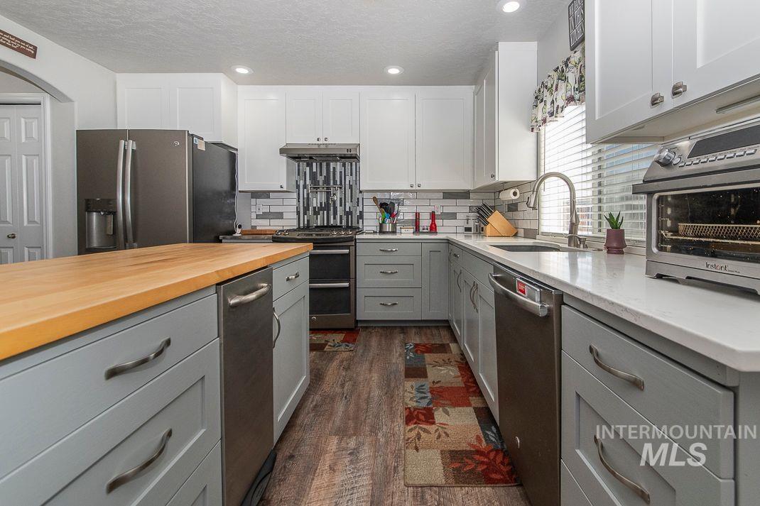 3013 Gala Trail Emmett, ID 83617 - Photo 6 of 22 Kitchen with custom gray cabinetry, stainless steel appliances, dark wood lvp floors and full tile backsplash