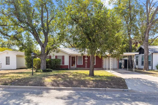 a view of a white house next to a yard with large trees