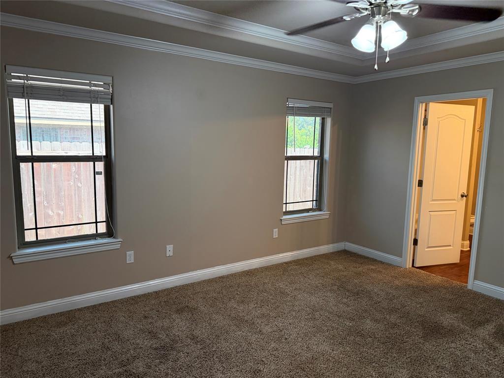 520 Big Red Circle Haughton, LA 71037 - Photo 12 of 25 Carpeted room featuring two windows with horizontal blinds, a ceiling fan with integrated lighting, a tray ceiling with crown molding, and an interior door leading to an additional space
