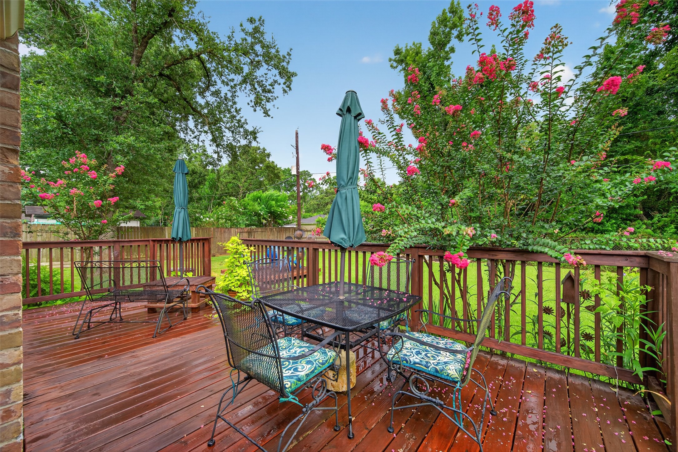 24719 Wilderness Road Spring, TX 77380 - Photo 37 of 42 This photo showcases a beautiful backyard deck with wooden flooring, surrounded by lush greenery and flowering plants. It features a perfect space for relaxation and entertaining.