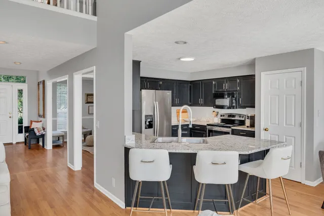 a kitchen with stainless steel appliances kitchen island granite countertop a dining table chairs and a refrigerator