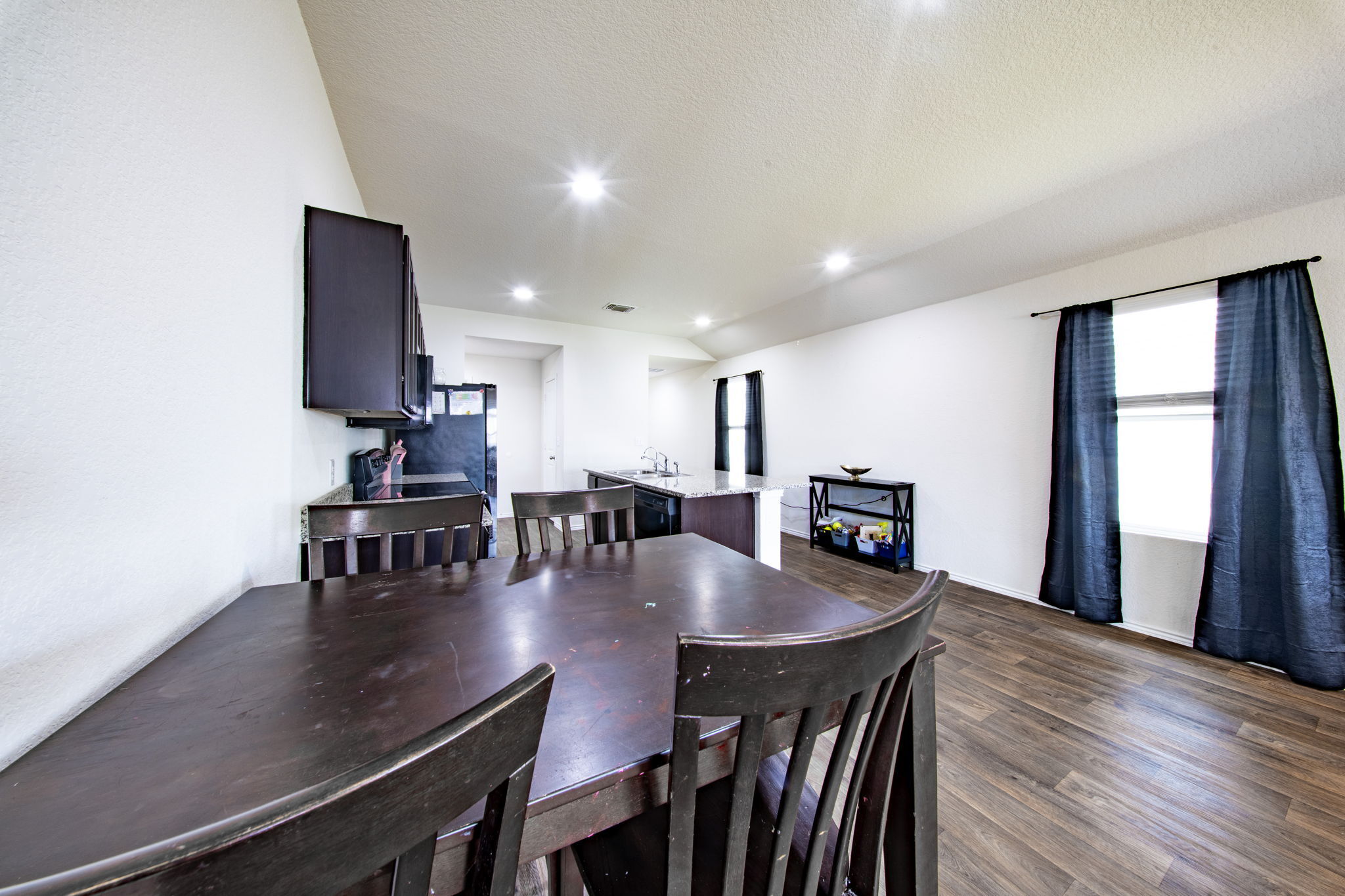 14903 Tuff Road Manor, TX 78653 - Photo 6 of 25 An open-concept living space integrates a functional kitchen with a bright dining area, featuring robust wood flooring.